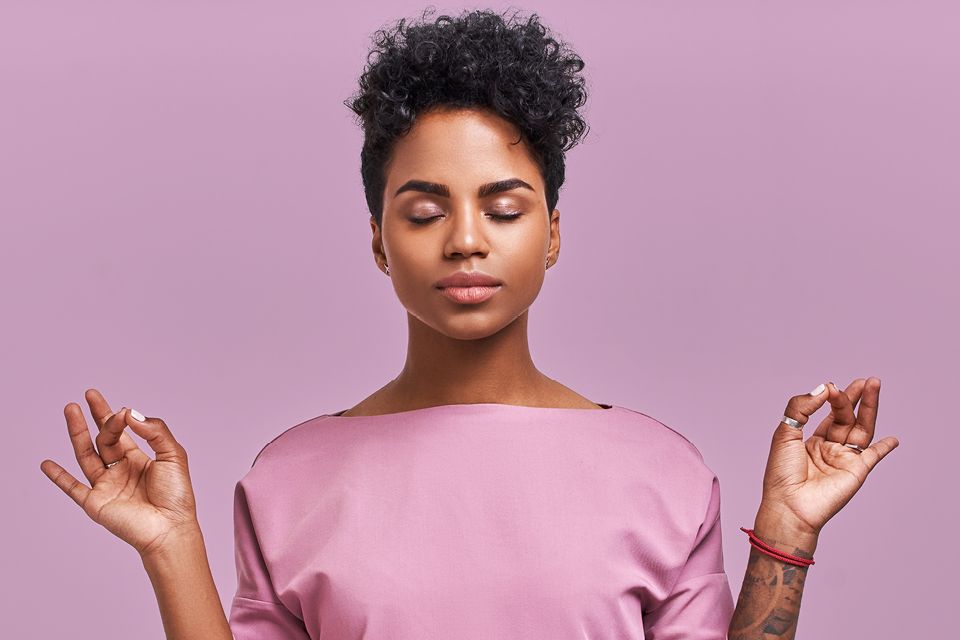 Black woman with hands raised and eyes closed in a calm state combatting stress.
